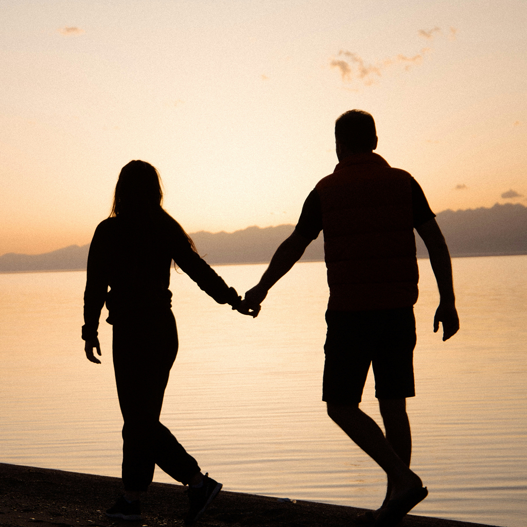 Couple walking holding hands along water